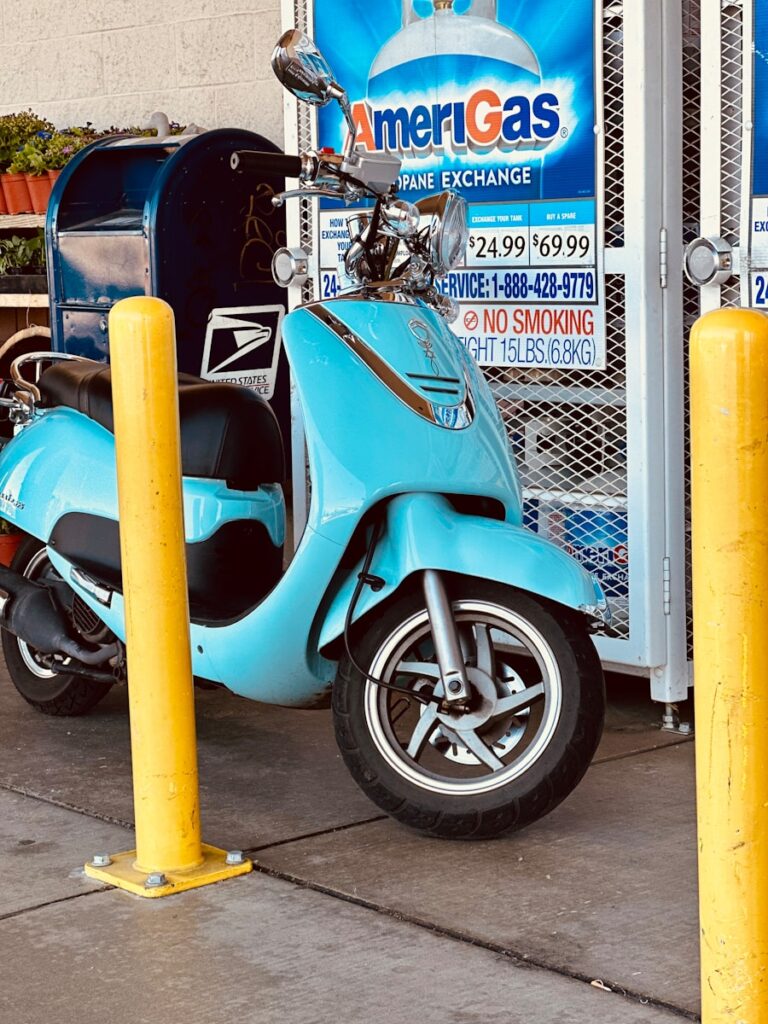 a blue scooter parked next to a yellow pole