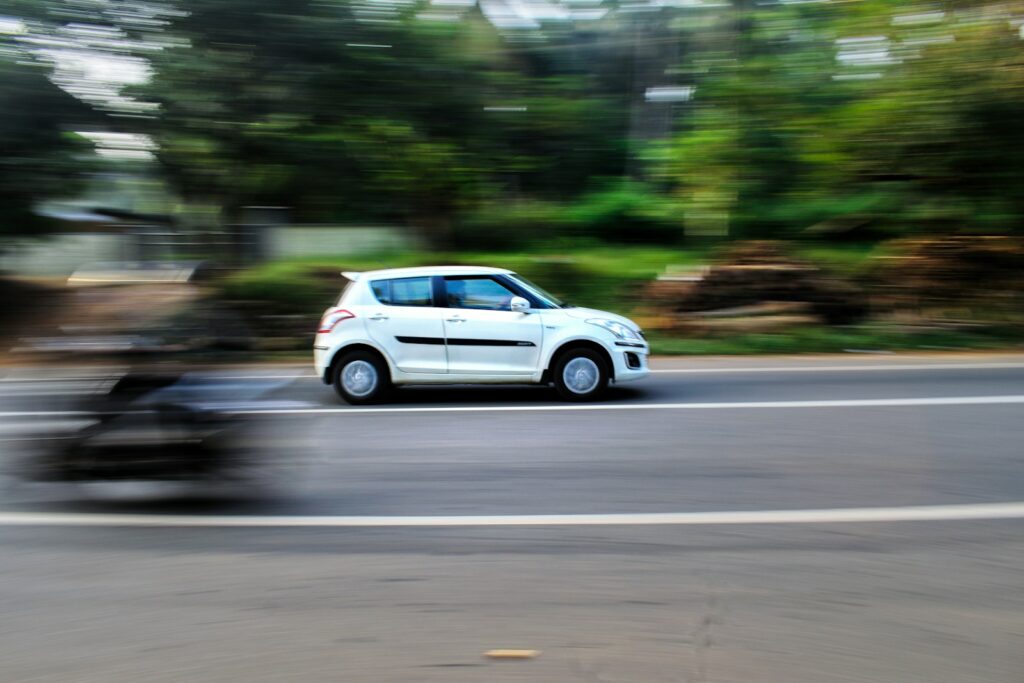 a white car driving down a street next to a forest
